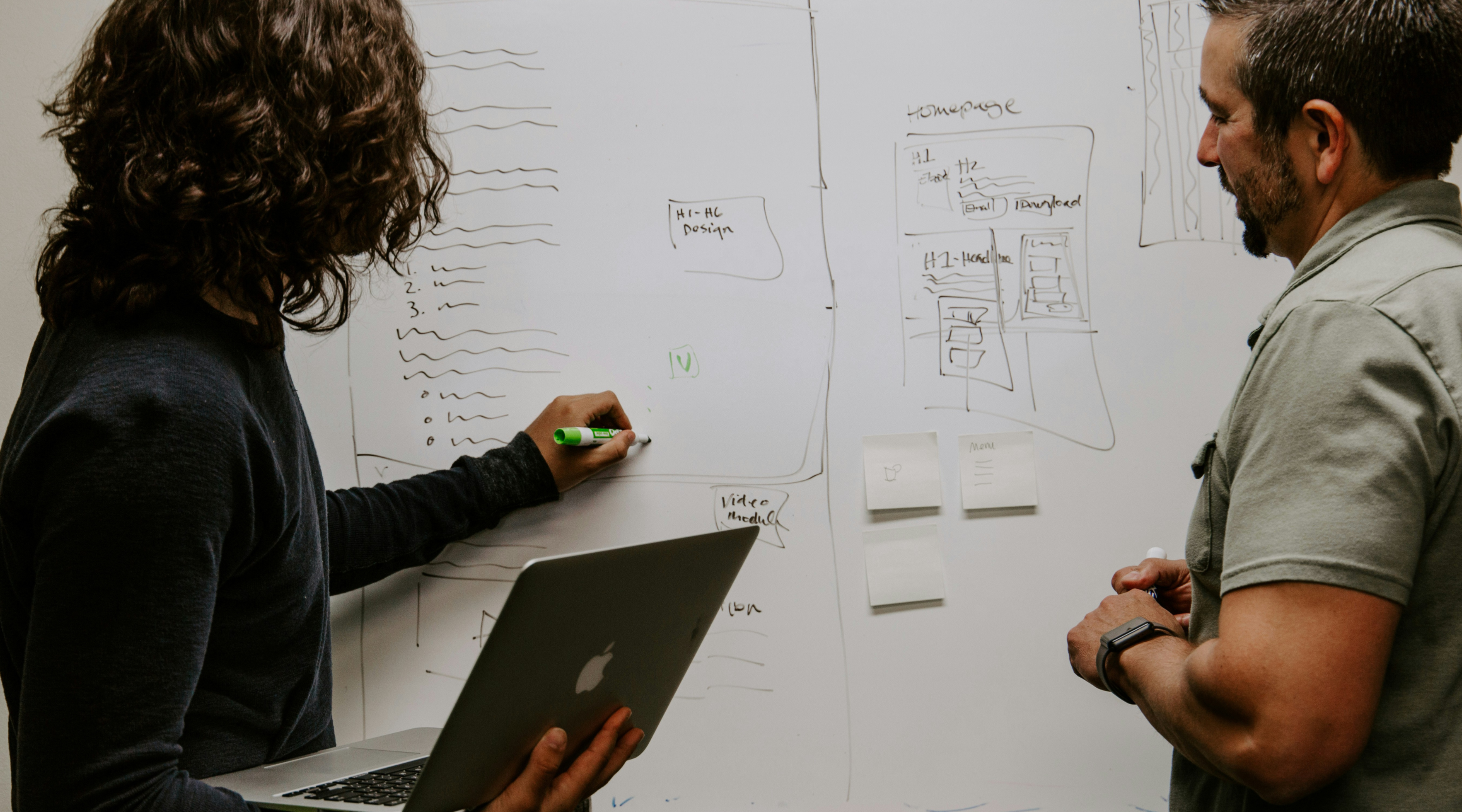 Image of an executive assistant writing on a dry erase board in front of colleague. 